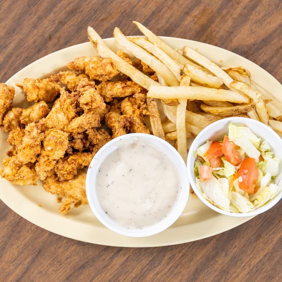 Plate of crispy fried chicken tenders, French fries, ranch dressing, and a side salad on a wooden table.