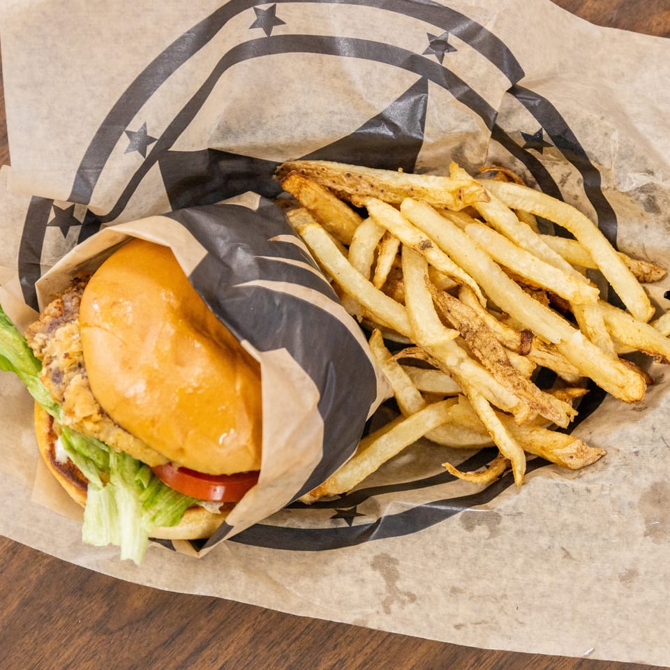 Crispy chicken sandwich with lettuce and tomato beside a generous serving of golden French fries on branded paper.