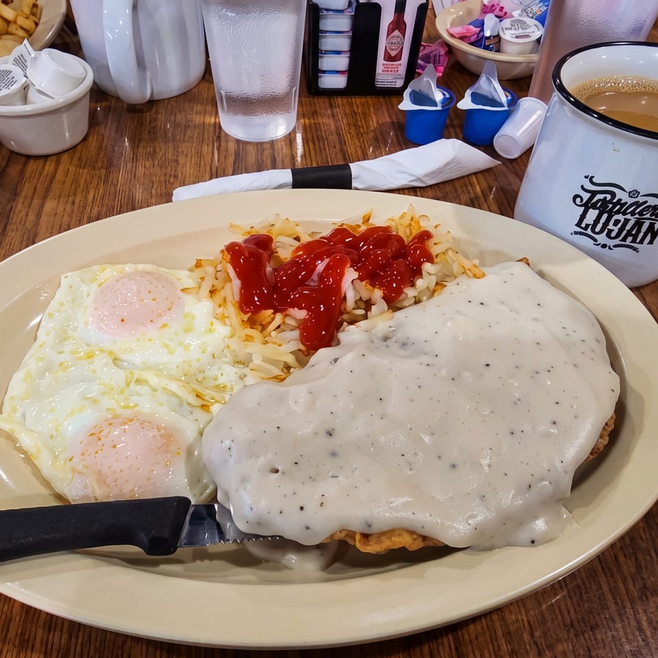 Diner plate with biscuits and gravy, two fried eggs, ketchup-covered hash browns, and coffee in an Arthur’s Cuban mug.