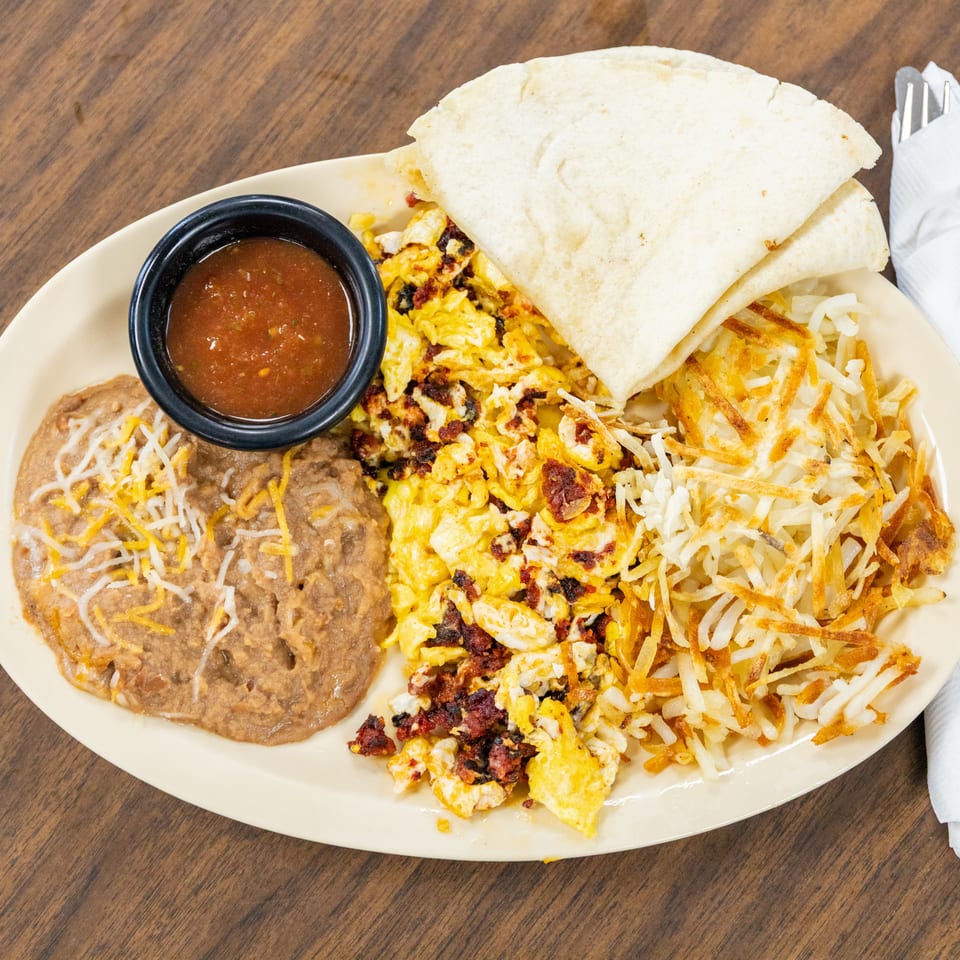 Mexican breakfast plate with scrambled eggs, bacon, hash browns, refried beans, tortillas, shredded cheese, and salsa.